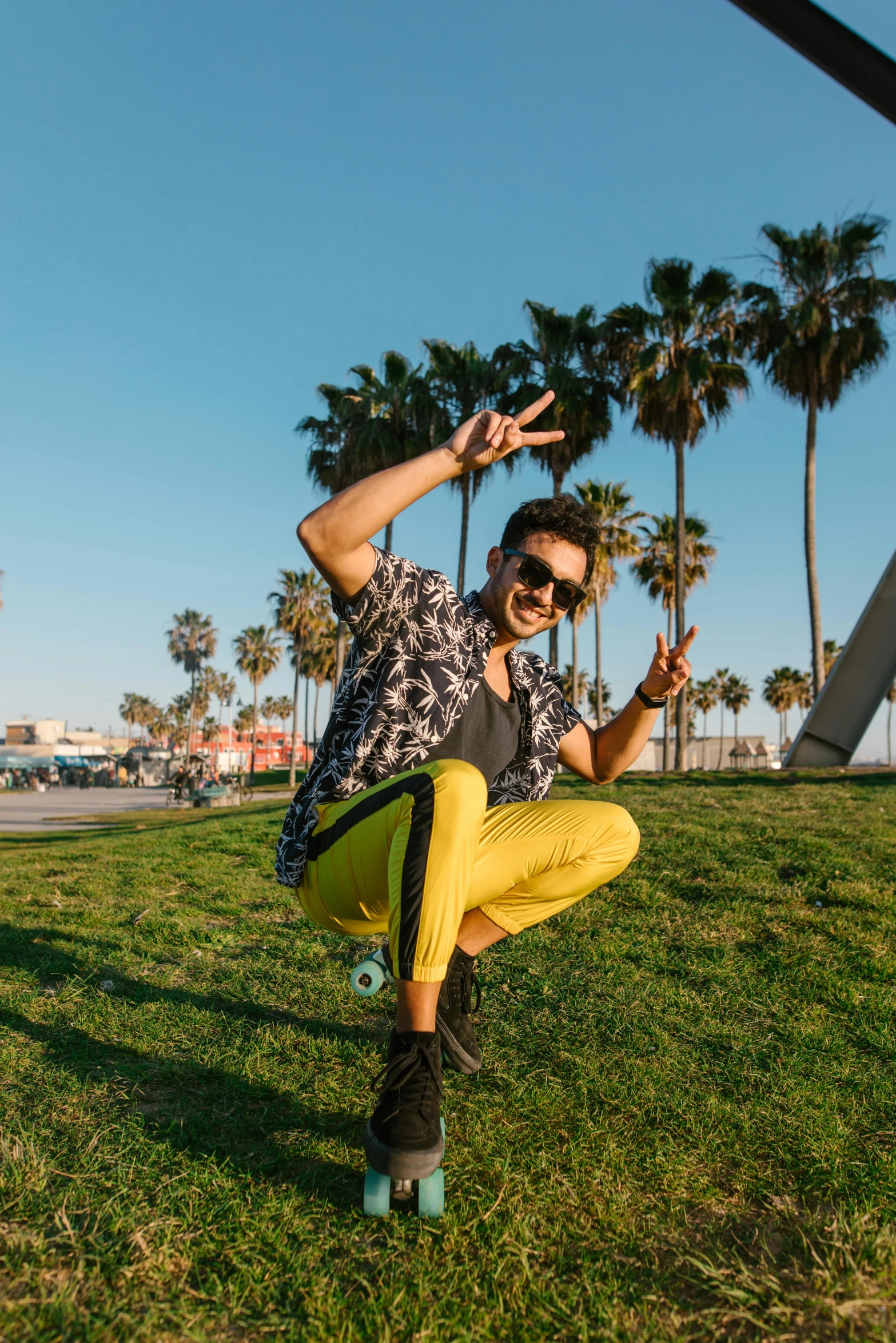 a man riding a skateboard on top of a lush green field, by Julia Pishtar, trending on unsplash, graffiti, bright trouser suit for a rave, palm trees, black and yellow tracksuit, avan jogia angel