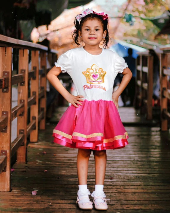 a little girl standing on a wooden bridge, a portrait, by reyna rochin, pexels, happening, dressed as a queen, pink skirt, thumbnail, girl wearing uniform