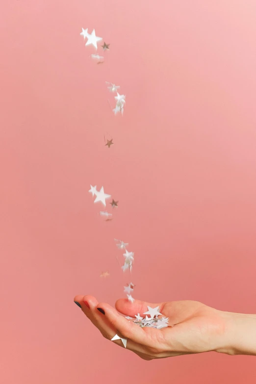 a person holding a star shaped object in their hand, inspired by Cerith Wyn Evans, trending on pexels, magical realism, pink background, flying fairies, paper decoration, tiny stars