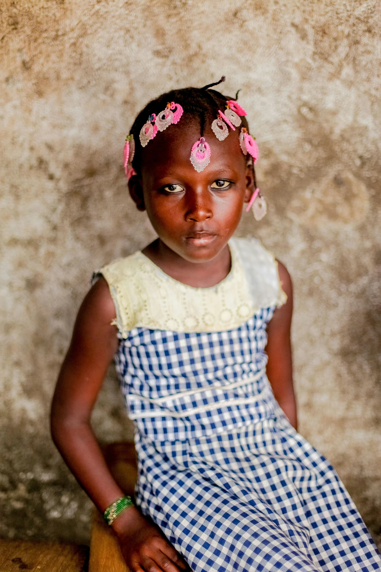 a little girl sitting on top of a wooden bench, by Daniel Gelon, african facial features, wearing a dress made of beads, 2022 photograph, young female