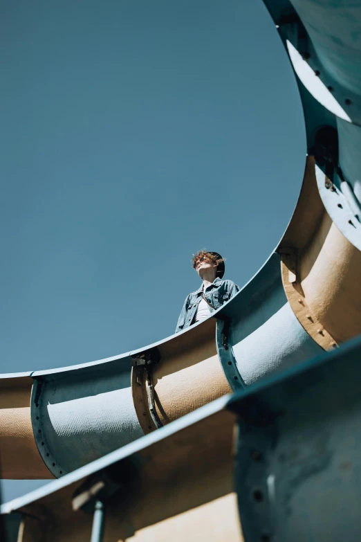 a man standing on top of a metal pipe, blue slide park, portrait featured on unsplash, declan mckenna, looking from slightly below