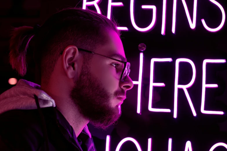 a man standing in front of a neon sign, trending on pexels, realism, jewish young man with glasses, bright pink purple lights, pondering, h3h3