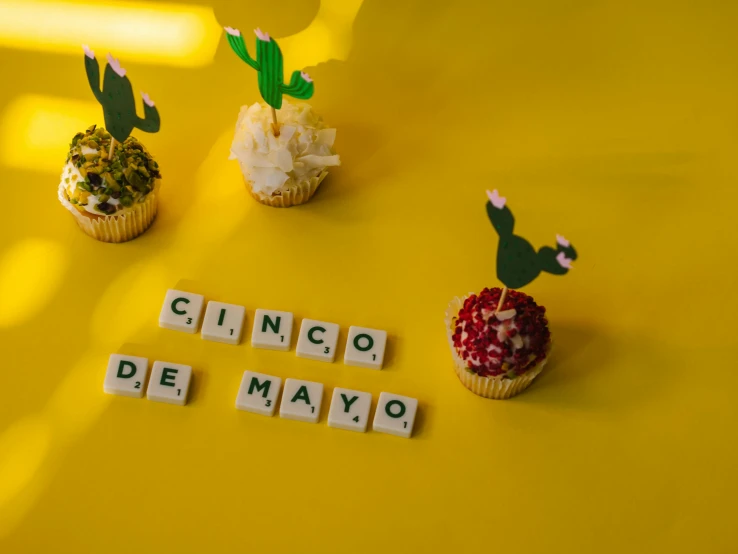 a couple of cupcakes sitting on top of a yellow table, she is mexican, cubes on table, in white lettering, may