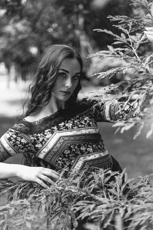 a black and white photo of a woman leaning against a tree, inspired by Andrei Ryabushkin, arabesque, patterned clothing, lilly collins, amongst foliage, andrey surnov