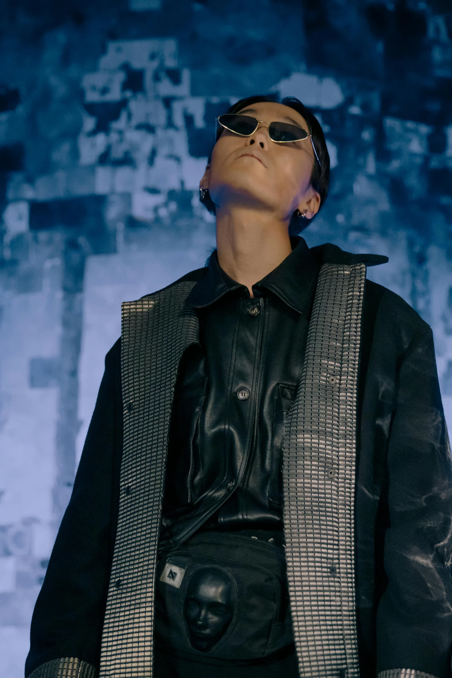 a man with sunglasses standing in front of a wall, an album cover, inspired by Tadashi Nakayama, trending on pexels, bauhaus, wearing a full leather outfit, performing a music video, brutalist fashion show, hito steyerl