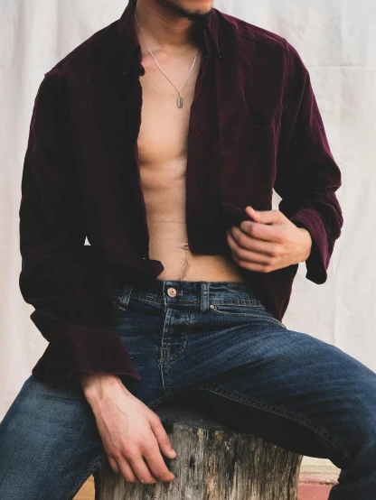 a shirtless man sitting on top of a tree stump, an album cover, by Nina Hamnett, trending on unsplash, renaissance, dressed in velvet, button up shirt, ( ( ( wearing jeans ) ) ), detail shot