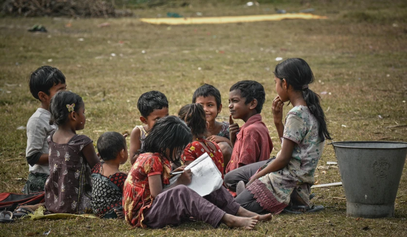 a group of children sitting on top of a grass covered field, by Jesper Knudsen, pexels contest winner, bengal school of art, village girl reading a book, group sit at table, from reading to playing games, indigenous