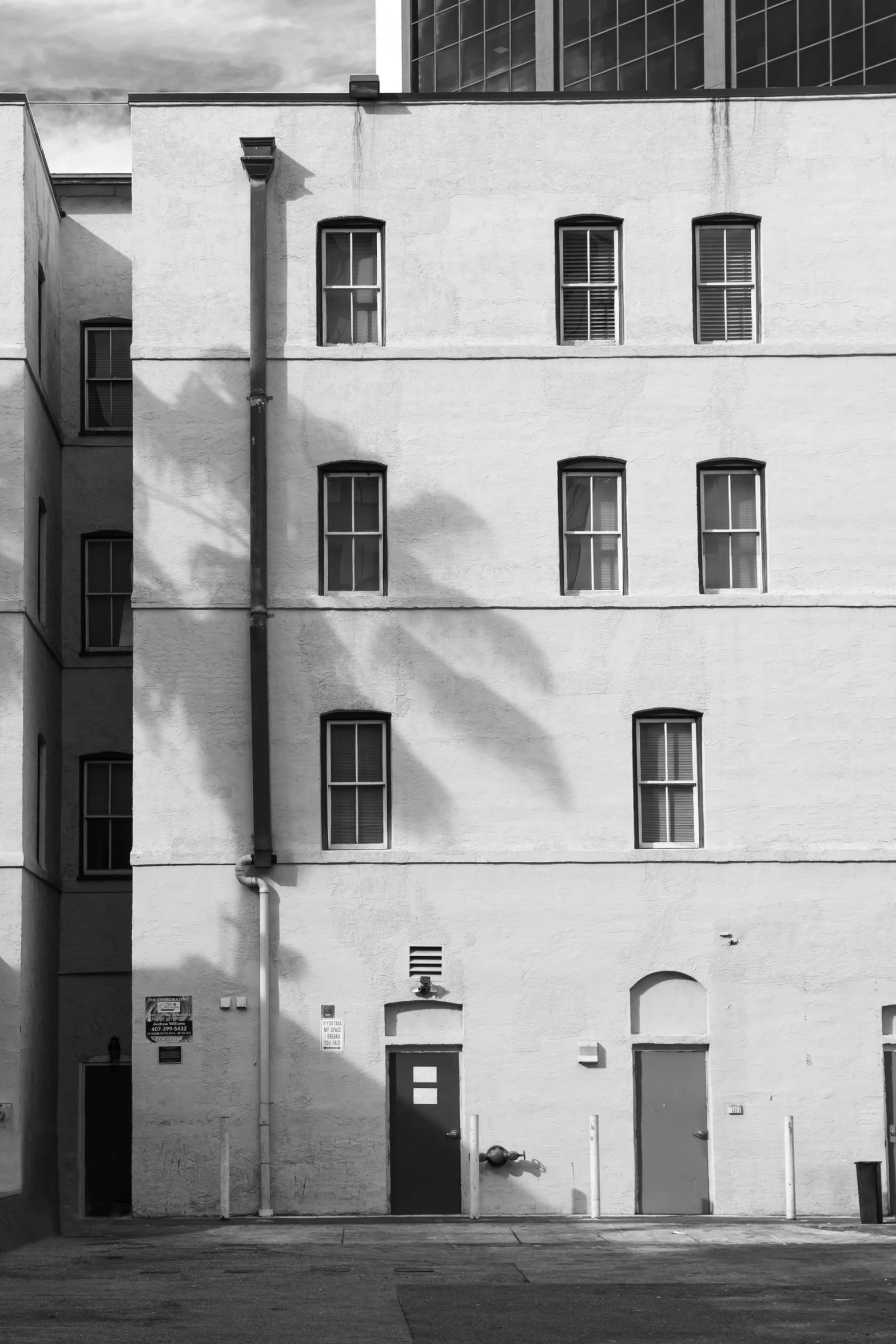 a black and white photo of a tall building, a black and white photo, inspired by André Kertész, unsplash, postminimalism, palm trees outside the windows, barracks, shady alleys, los angeles 2 0 1 5