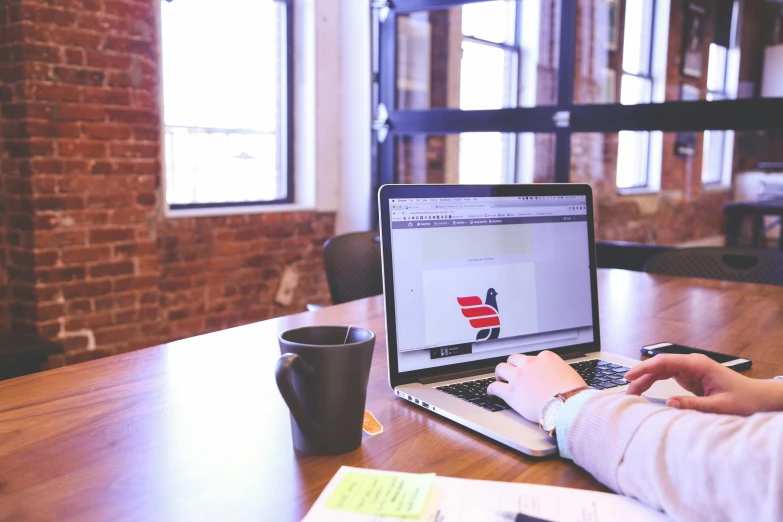 a person sitting at a table working on a laptop, pexels contest winner, 9 9 designs, background image, in an office, no - text no - logo