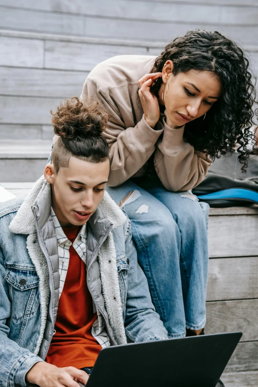 a man and woman sitting on steps looking at a laptop, trending on pexels, antipodeans, lesbians, brown curly hair, heartbreaking, wearing a jeans jackets