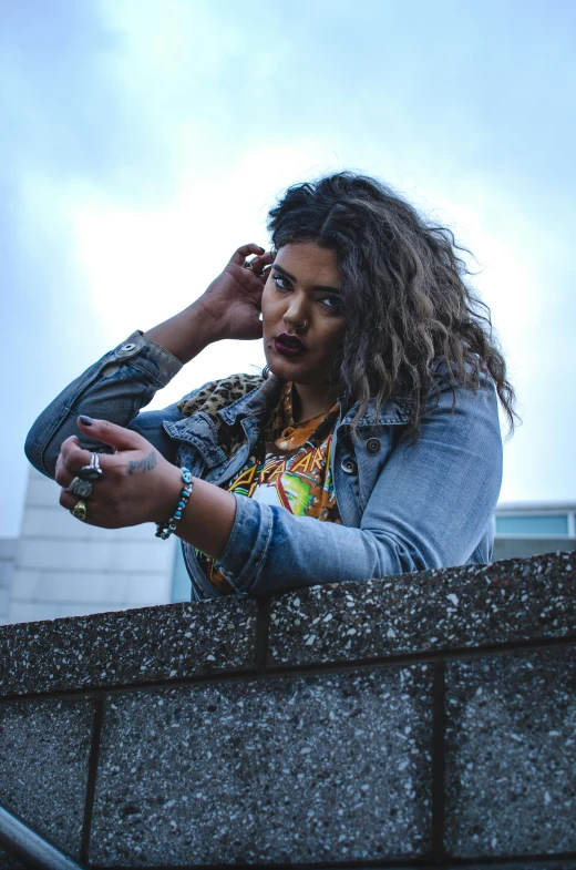 a woman standing on a ledge talking on a cell phone, an album cover, trending on pexels, graffiti, alluring plus sized model, provocative indian, she wears a jacket, nonbinary model