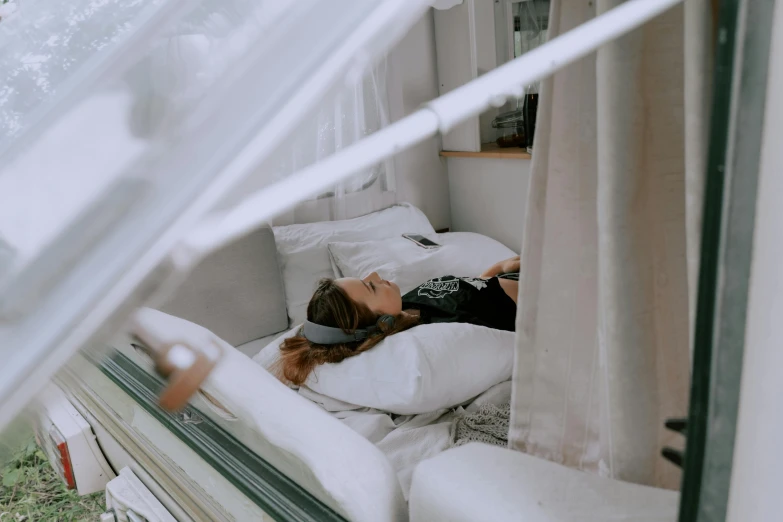 a woman laying on a bed in a camper, pexels contest winner, inside a glass box, white limbo, very comfy], covered with wires