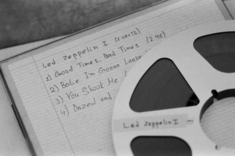 a film reel sitting on top of a piece of paper, an album cover, led zeppelin, found written in a notebook, grainy black and white footage, good times