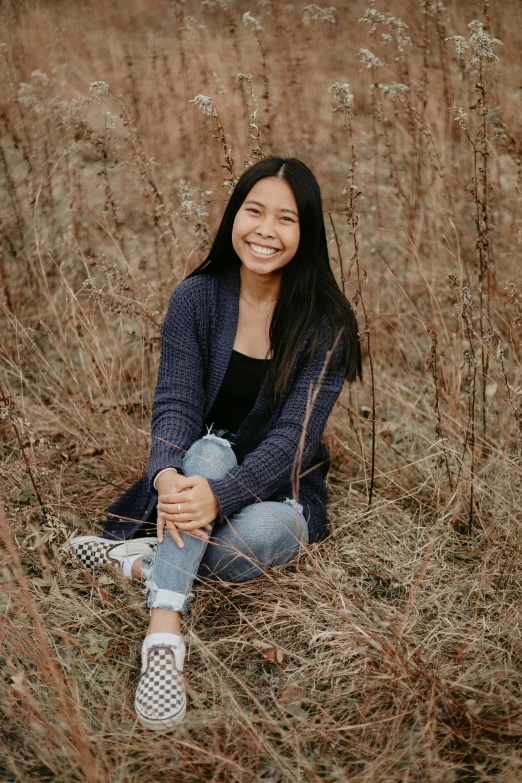 a woman sitting in a field of tall grass, a picture, pexels contest winner, smiling down from above, asian descent, in a navy blue sweater, standing on rocky ground