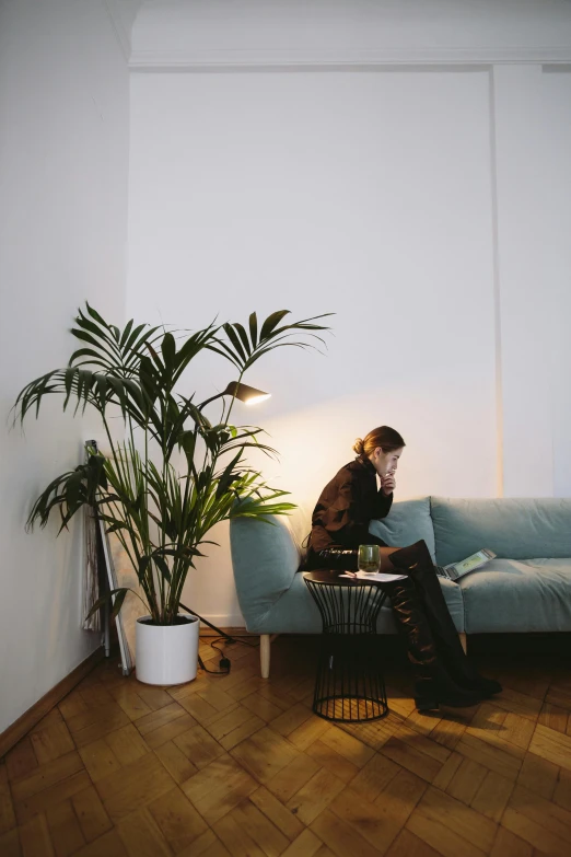 a woman sitting on a couch next to a potted plant, inspired by Elsa Bleda, trending on unsplash, minimalism, trying to study, kreuzberg, low quality photo, light lighting side view