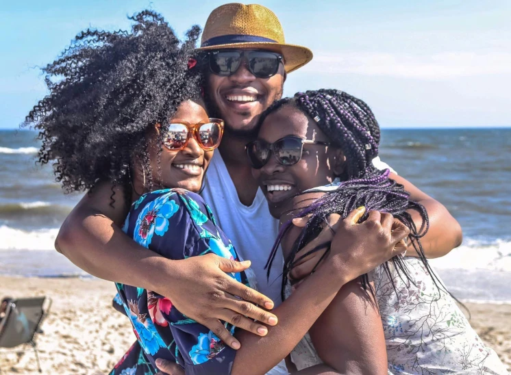 a group of people standing on top of a sandy beach, black skin, smiling couple, woman holding another woman, road trip exciting