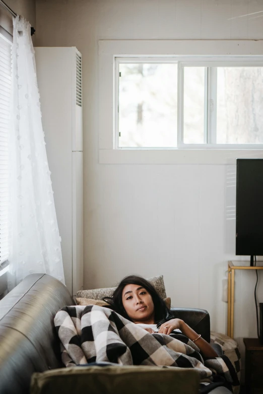 a woman laying on a couch in a living room, by Everett Warner, trending on pexels, asian descent, sick with a cold, low quality photo, window