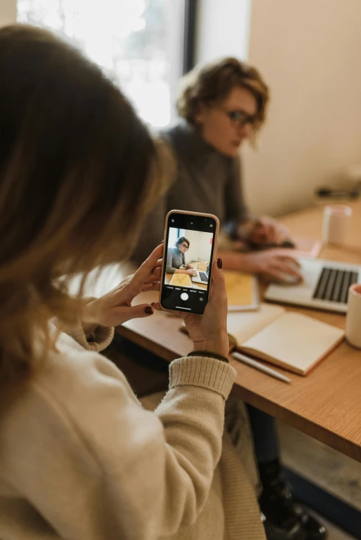 a woman sitting at a table using a cell phone, a picture, trending on pexels, coworkers, two still figures facing camera, instagram digital, brown