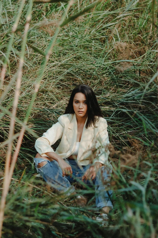 a woman sitting in a field of tall grass, an album cover, by Sebastian Vrancx, chloe bennet, portrait image, white shirt and jeans, looking serious