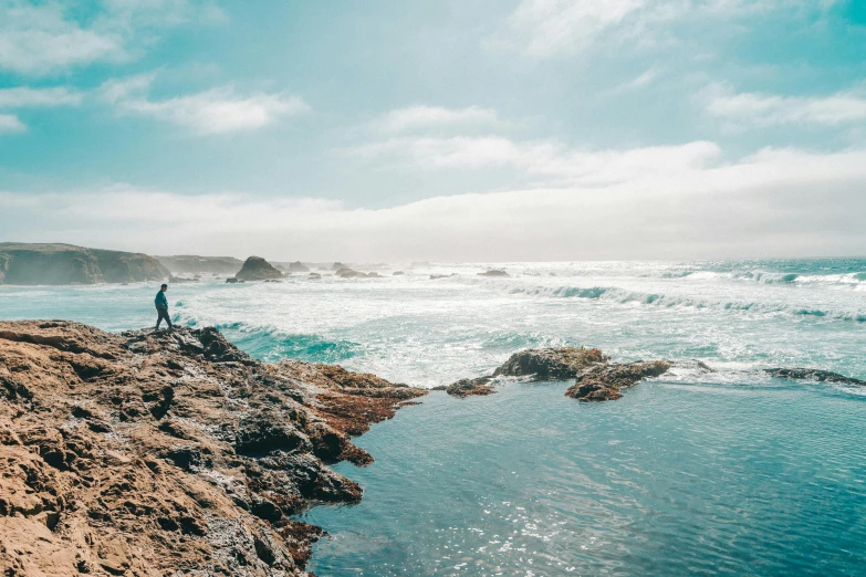 a man standing on the edge of a cliff overlooking the ocean, a photo, by Ryan Pancoast, pexels contest winner, process art, rock pools, light blue water, bay area, youtube thumbnail