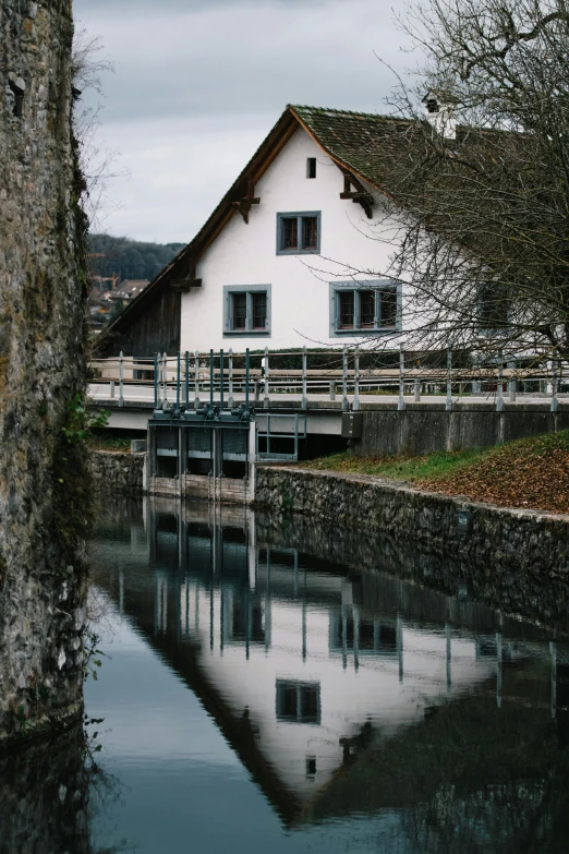 a white house sitting next to a body of water, a picture, inspired by Karl Stauffer-Bern, renaissance, mill, medium format. soft light, gray, chalet