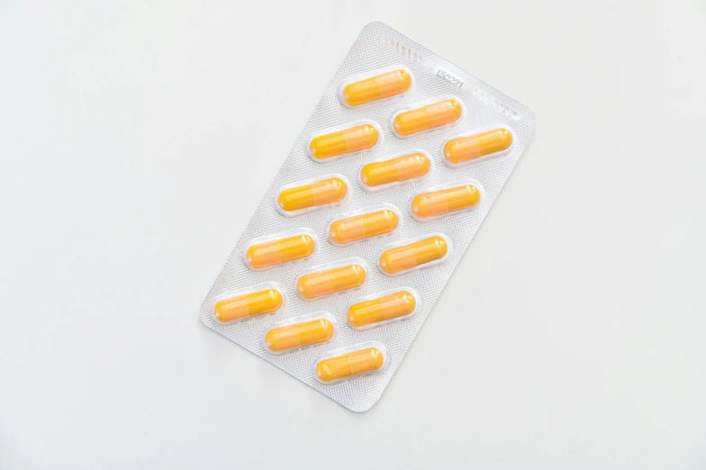 a pack of orange pills sitting on top of a white table, by Nina Hamnett, rounded corners, mono-yellow, processor, product view