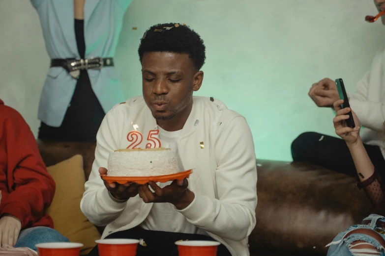 a man blowing out a candle on a cake, pexels, hyperrealism, 2 1 savage, 2 5 th anniversary music video, black teenage boy, a group of people