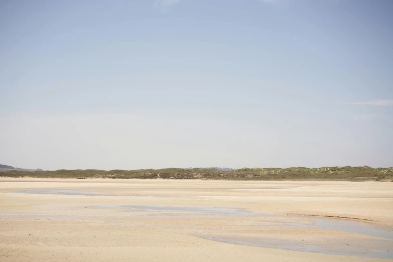 a man flying a kite on top of a sandy beach, by Liza Donnelly, unsplash, minimalism, landscape of flat wastelands, on the beach at noonday, seen from a distance, cloudless-crear-sky