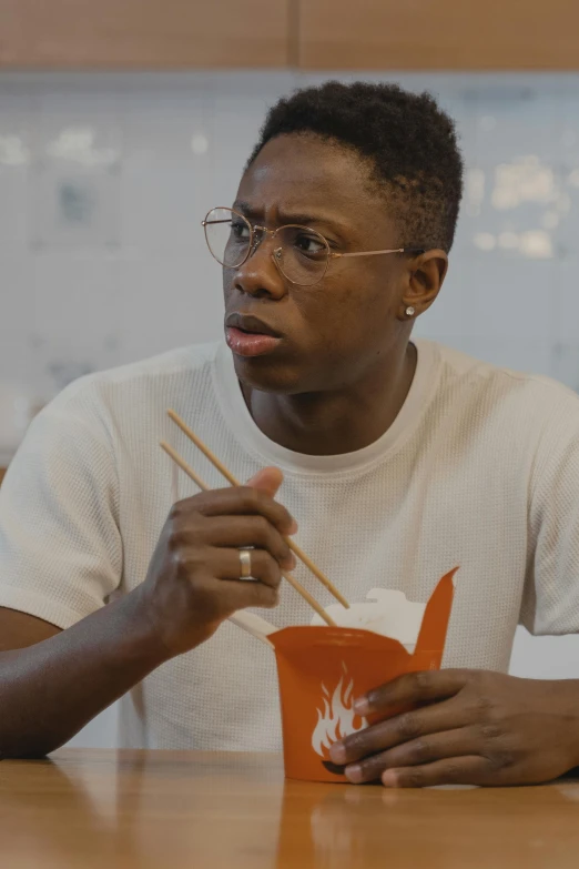 a man sitting at a table with chopsticks in his hand, trending on reddit, black teenage boy, in a taco bell, looking confused, wearing thin large round glasses