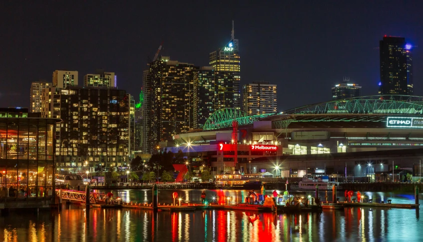 a large body of water with a city in the background, by Tom Phillips, pexels contest winner, victorian harbour night, entertainment district, dingy, neon signs in background