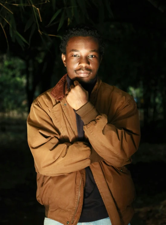a man in a brown jacket posing for a picture, an album cover, by Nyuju Stumpy Brown, unsplash, portrait soft low light, ( ( dark skin ) ), aged 2 5, dolman