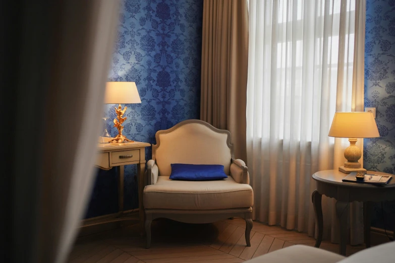 a chair sitting in front of a window next to a lamp, inspired by Alexander Roslin, rococo, brilliant royal blue, hotel room, elegant fabric, medium-shot