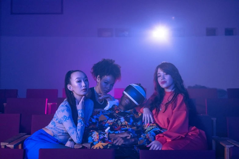 a group of people sitting next to each other in a theater, an album cover, inspired by Zhu Da, unsplash, colourful clothing, womanhood”, 35mm dramatic lighting, filmstill