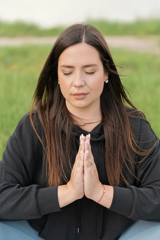 a woman sitting in the grass with her eyes closed, blessing hands, wearing a black hoodie, sukhasana, profile image