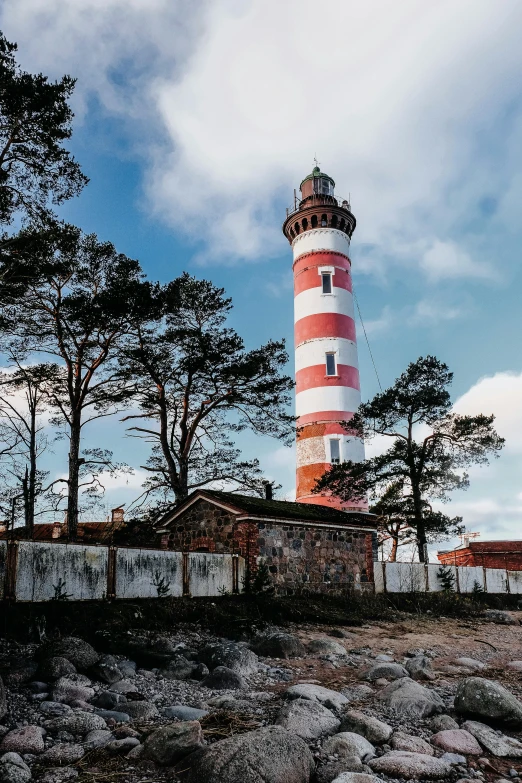 a red and white lighthouse sitting on top of a rocky beach, rutkowskyi, profile image, trees around, multiple stories