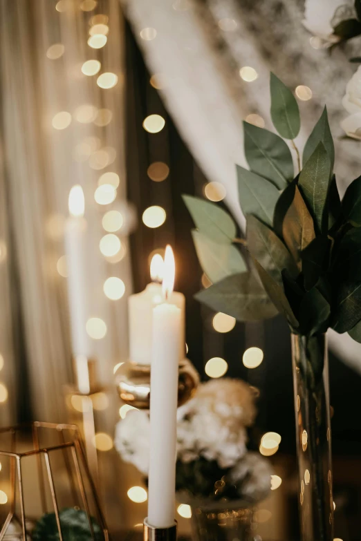 a couple of candles sitting on top of a table, subtle gold accents, fairy lights, indoor setting, moody hazy lighting