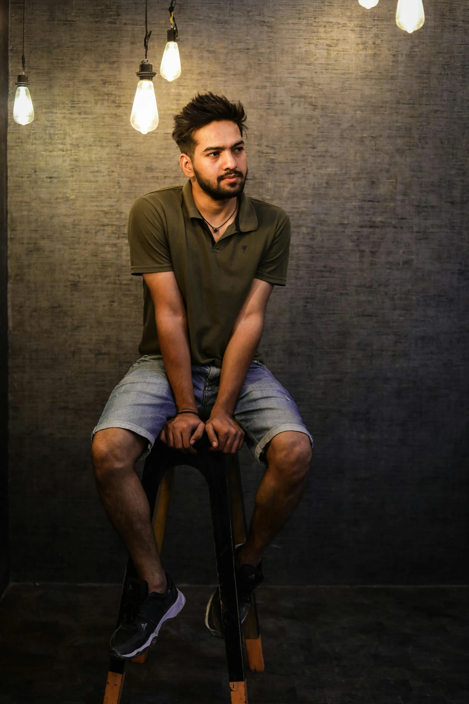 a man sitting on a stool in a dark room, a portrait, inspired by Saurabh Jethani, pexels contest winner, hurufiyya, in front of white back drop, casual pose, scruffy looking, young adult male