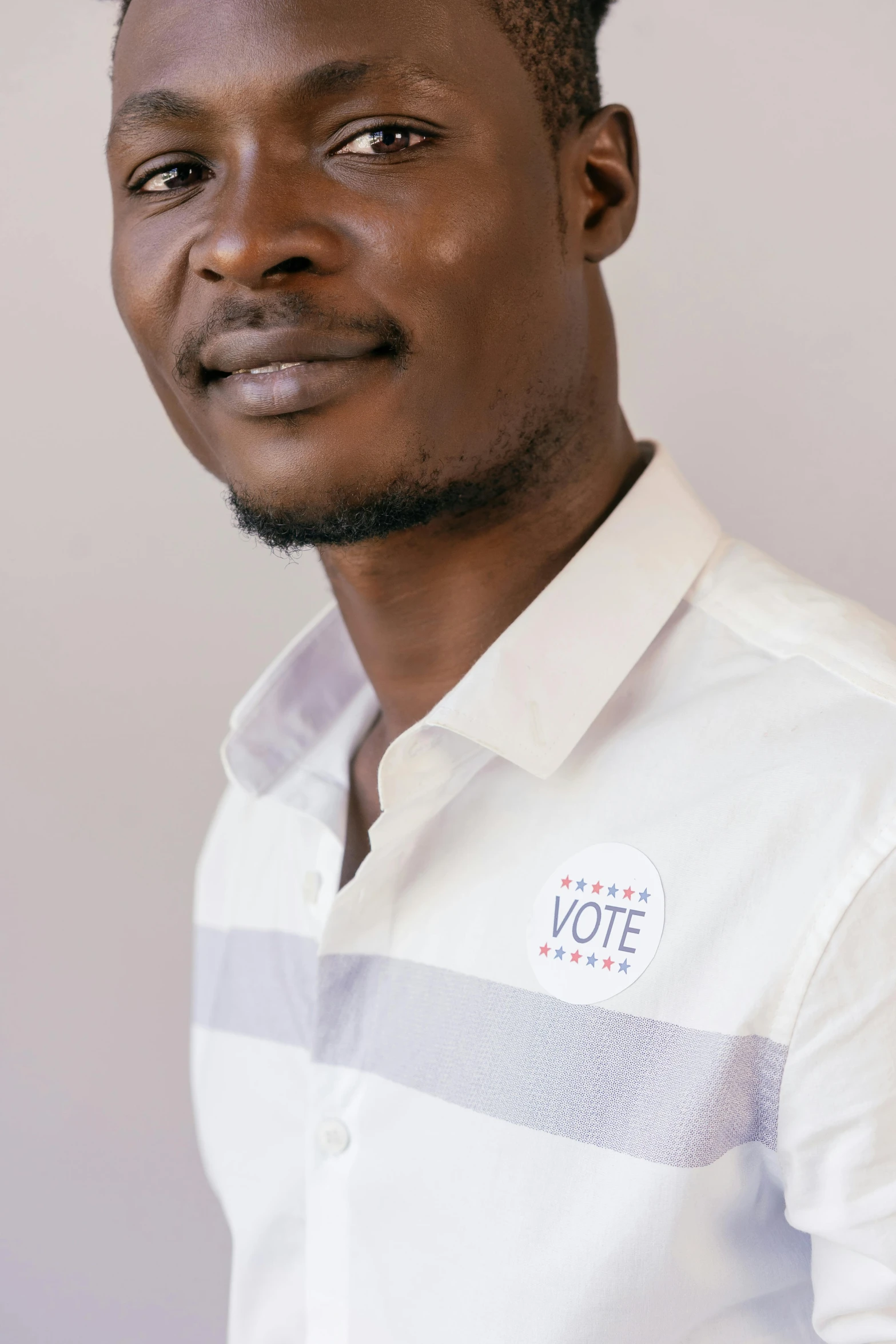 a man standing in front of a white wall, by Chinwe Chukwuogo-Roy, pexels contest winner, election poster, headshot profile picture, wearing a light shirt, hannah yata