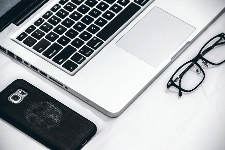 an open laptop computer sitting on top of a bed, trending on pexels, black rimmed glasses, silver accessories, background image, white and black