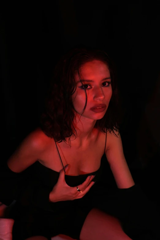 a woman in a black dress sitting on a bed, an album cover, inspired by Nan Goldin, trending on pexels, realism, red neon eyes, zendaya, concert, profile pic