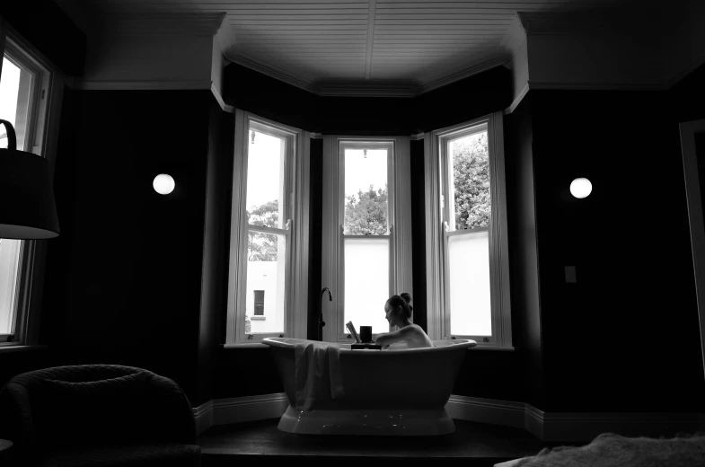 a black and white photo of a person in a bathtub, inspired by Carrie Mae Weems, unsplash, bay window, wellington, hotel room, inside a grand