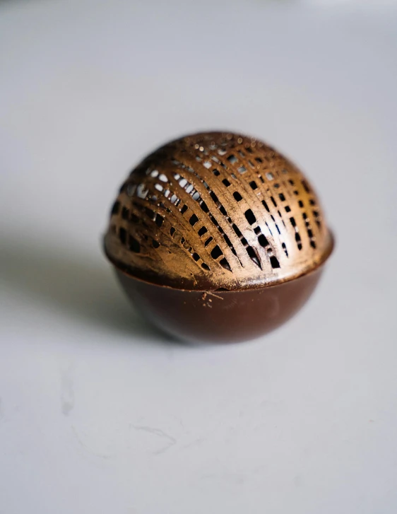 a close up of a metal object on a table, fully chocolate, ball shaped accordion sleeve, gold speckles, product shot