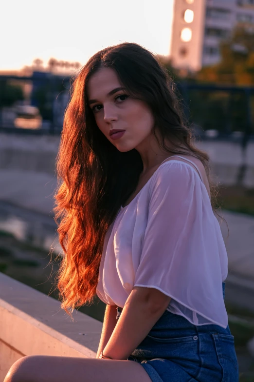 a woman sitting on a ledge looking at the camera, inspired by Elsa Bleda, pexels contest winner, renaissance, long brown wavy hair, summer evening, loosely cropped, backlight photo sample