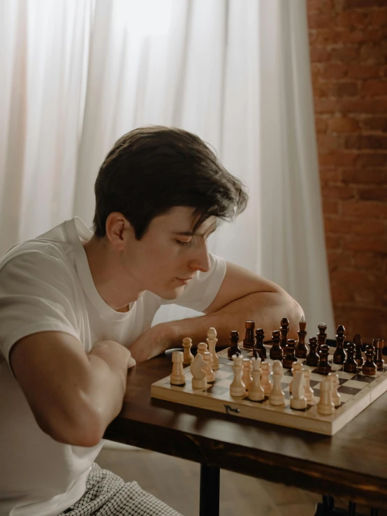 a man sitting at a table playing a game of chess, an epic non - binary model, profile image, smooth pale skin, declan mckenna