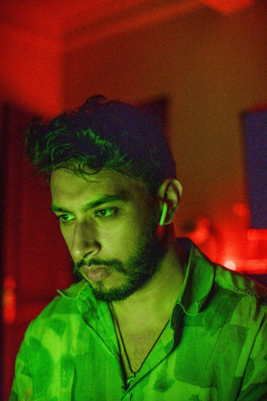 a man sitting in front of a laptop computer, an album cover, inspired by Elsa Bleda, trending on pexels, green body. red eyes, provocative indian, bisexual lighting, headshot profile picture