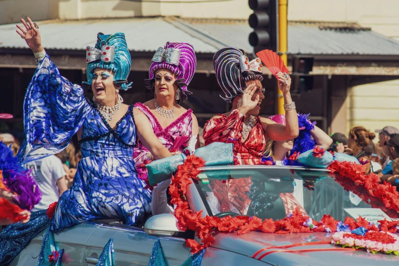 a group of women riding in the back of a car, by Lee Loughridge, pexels contest winner, renaissance, magic parade float, manly, teal silver red, wearing floral chiton