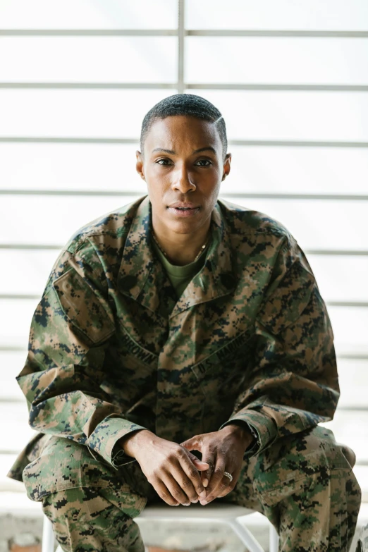 a man in a military uniform sitting on a chair, by Alison Geissler, mixed-race woman, slide show, lesbians, looking serious