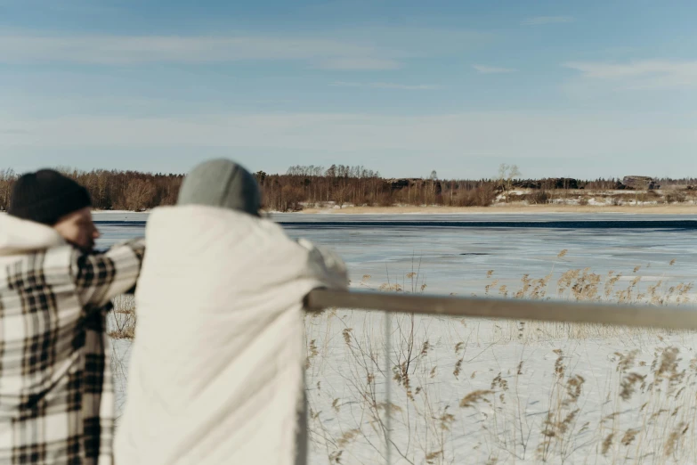 two people looking out over a frozen lake, inspired by Eero Järnefelt, unsplash, covered with blanket, low quality footage, sunny day time, cinematic shot ar 9:16 -n 6 -g