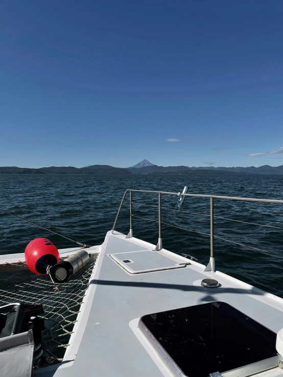 a red buoy sitting on the bow of a boat, a picture, by Jessie Algie, purism, with a volcano in the background, cockpit view, panorama shot, taken in 2022