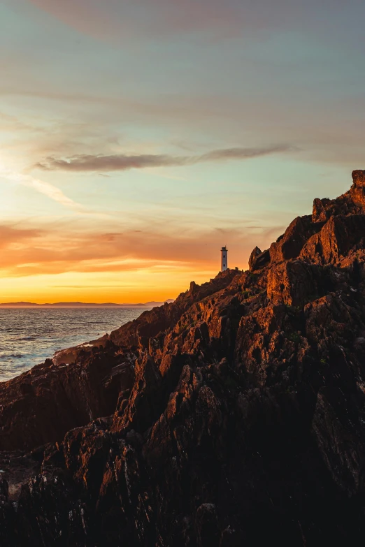 a lighthouse sitting on top of a rocky cliff next to the ocean, at the golden hour, craggy mountains, fire lit